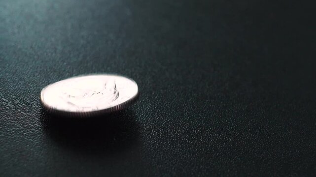 extreme closeup of a quarter dropping and spinning to halt, the coin faces the viewer when it stops.