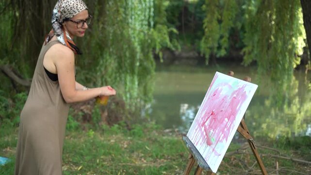 Beautiful woman artist painting on a canvas by the river in a dress