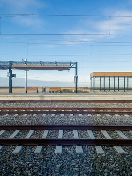 Train station scene with parallel tracks and an empty platform under a bright blue sky, conveying travel, transportation, and calm anticipation of journeys ahead.