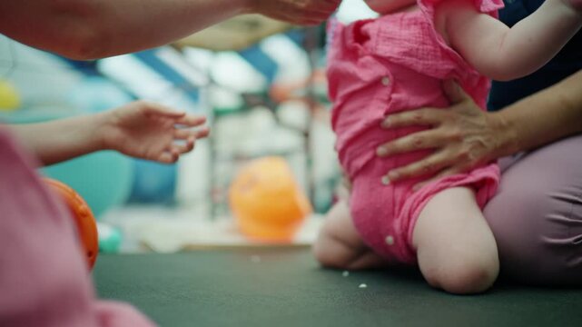 Young infant girl attempting to crawl, parent's hand supporting her, offering a pacifier for comfort