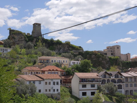 View of the historic Kruje Castle overlooking the town with traditional stone houses, red-tiled roofs, and lush green hills in Kruje, Durres County, Albania.