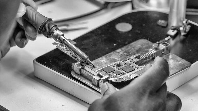 Close-up technician repairing small laptop circuit board in electronics workshop