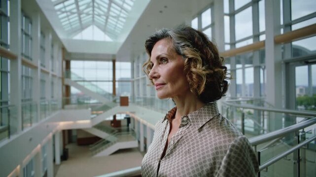 Noticing skylight, woman in patterned top raising hand and pointing upward from atrium railing