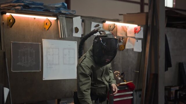 Young adult Caucasian male welder putting on protective helmet with air respirator system and heavy safety gloves in workshop. Footage is perfect for industrial manufacturing promotions