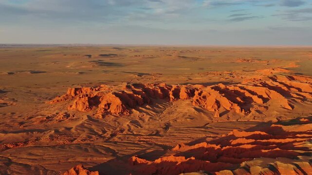 Aerial view of the red sandstone formations of the Flaming Cliffs at sunset, casting long shadows across the desert landscape in Bulgan, Omnogovi, Mongolia.
