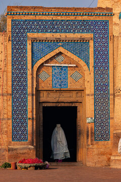 View of the intricate blue tile work and brick architecture at the entrance of the Tomb of Hazrat Shah Rukn-e-Alam with a person in a white veil entering in Multan, Punjab, Pakistan.