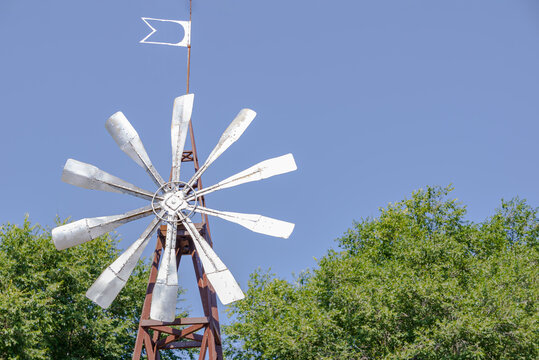 Vintage metal windmill with weather vane against clear blue sky in rural farm setting, agriculture and renewable energy concept