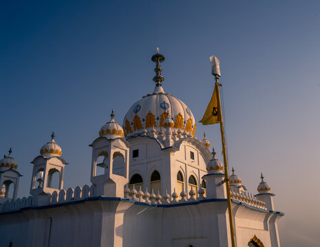 View of Gurdwara Shaheed Gunj Landa Bazar Lahore with its white dome, golden architectural details, and a yellow flag against a clear blue sky in Lahore, Punjab, Pakistan.