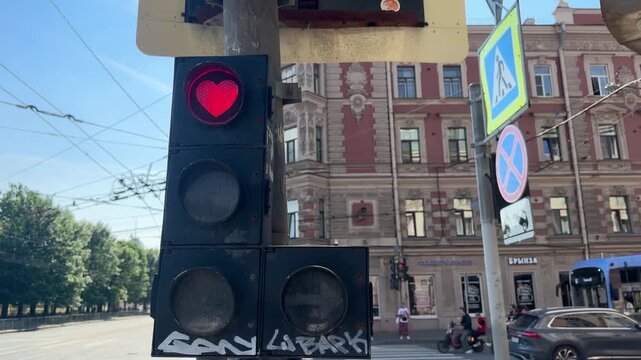 Red heart-shaped pedestrian traffic signal glowing on a city street. Urban transportation safety, public infrastructure, historic architecture, and love concept.