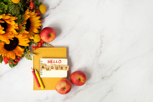 hello august text. bouquet with sunflowers, notepad, pencils, book and red apples on marble table background. august month calendar concept. summer end seasonal composition. flat lay. copy space