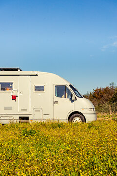 Camping car rv parked close to spring meadow with yellow flowers with blue sky during daytime