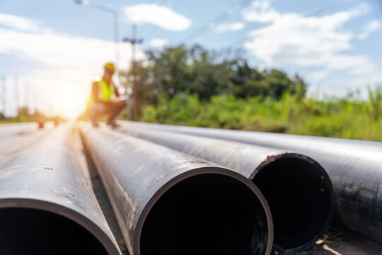 Large HDPE water supply pipes prepared for roadside installation with a worker inspecting the site, representing pipeline construction, utilities and water infrastructure.