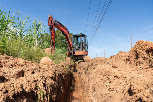 Excavator preparing a trench for underground water pipe installation along a roadside, representing pipeline construction, civil engineering and water infrastructure development.