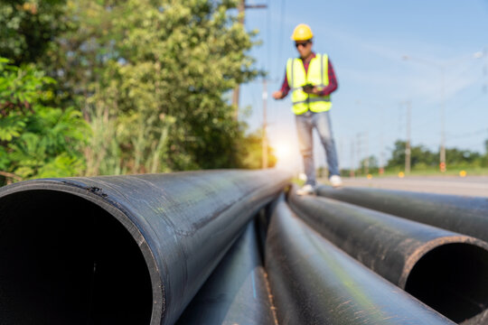 An Engineer inspecting large HDPE water supply pipes prepared for roadside installation, pipeline construction and public utility infrastructure development.