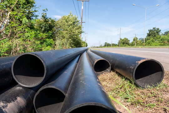 Large HDPE water supply pipes prepared for installation along roadside, pipeline construction materials for water distribution and public utility infrastructure project.