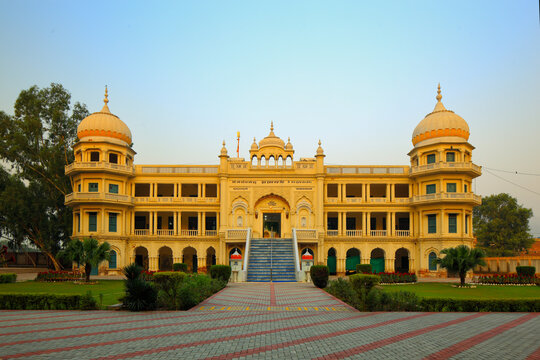 View of the historic Gurudwara Sacha Sauda with its yellow facade, prominent domes, and central staircase in Farooqabad, Punjab, Pakistan.