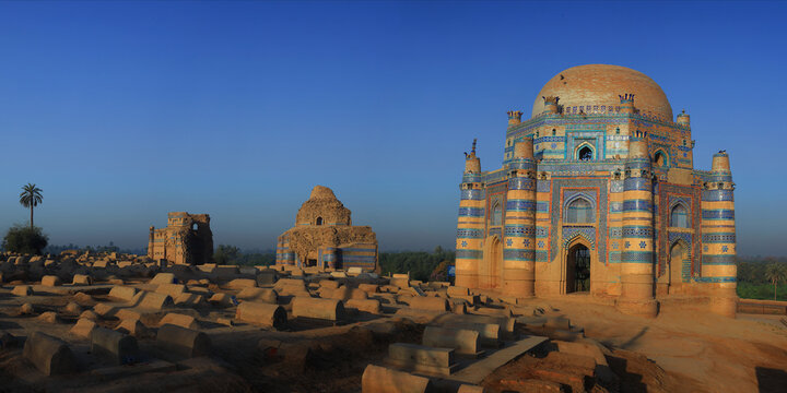 View of the historic Tomb of Javindi Bibi with its intricate blue tile work and surrounding ancient graves in the desert landscape of Uch Sharif, Punjab, Pakistan.