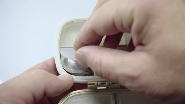 Hands opening pill organizer with tablets inside close up medication storage