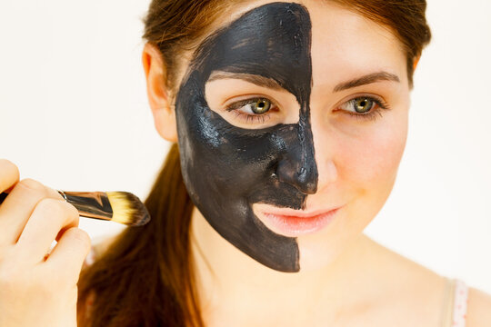 Female applying black mud facial mask