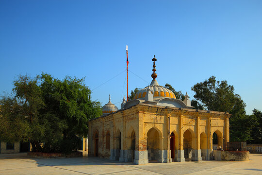 View of the historic Gurudwara Sacha Sauda with its yellow brick facade, arched entrances, and dome set against a clear blue sky in Farooqabad, Punjab, Pakistan.