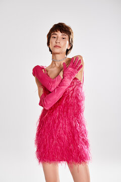 Stylish woman in pink feather dress and gloves poses elegantly in studio