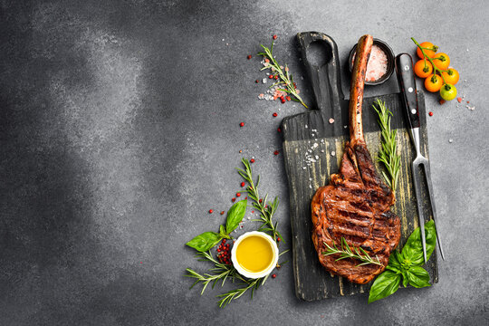 Beef steak on the bone. Grilled tomahawk steak with rosemary and spices on a cutting board. Top view. Free space for text.