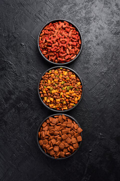 Black ceramic bowls with food for dogs and cats. On a black stone background. Free space for text.