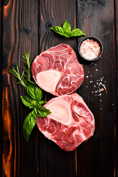 Raw aged ossobucco steak with spices and rosemary is ready to cook. On wooden background, top view.