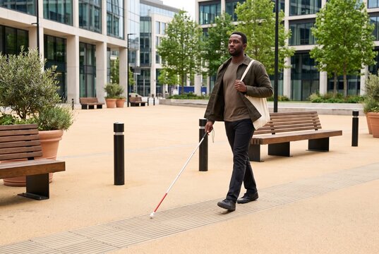 Blind man walking confidently with a white cane across a bright modern public square