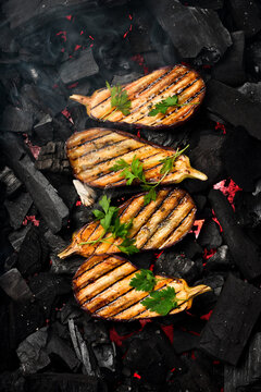Eggplants grilled on a metal grid. Hot coals. Top view. On a dark background.