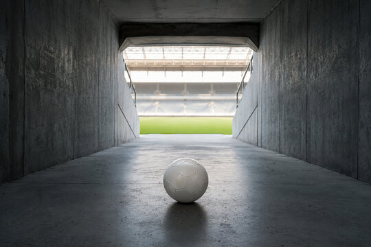 Lone football rests in concrete stadium tunnel leading toward a bright green pitch