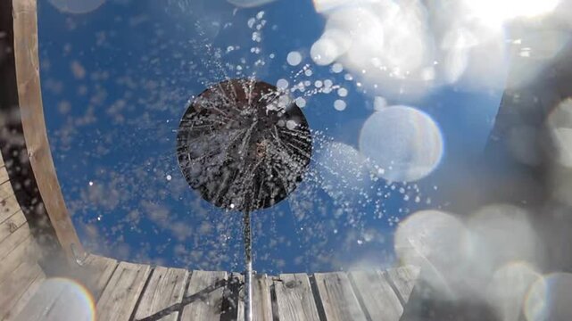 Water drops spraying from an outdoor shower head, creating a refreshing splash against a bright blue summer sky