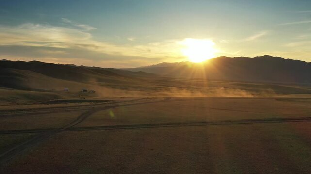 Aerial view of Baga Gazariin Chuluu landscape at sunset with distant ger tents and dust in the air in Dundgovi, Mongolia.