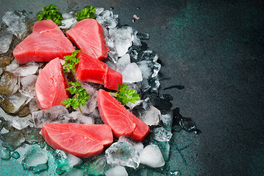 Fresh raw tuna fillet on ice cut into steak on a stone background with seasonings and herbs