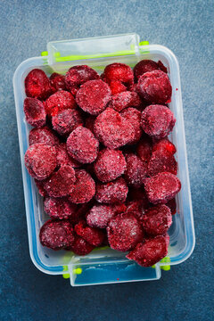 Frozen cherries in a plastic box. Preparation of frozen berries for the winter. On a gray stone background. Close-up.