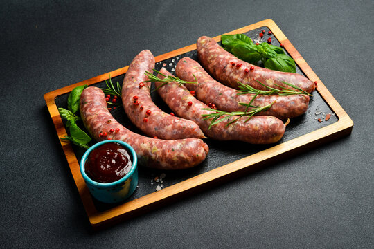 Raw beef sausages with rosemary and spices, ready to be grilled. On a wooden cutting board. Close up.