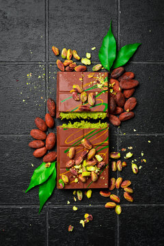 Trend Dubai chocolate with pistachio paste and kataifi. Pistachios, cocoa beans and chocolate. Top view, on a black stone background.