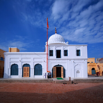 View of Gurudwara Patti Sahib with its white facade, arched doorways, and orange flag against a bright blue sky in Nankana Sahib, Punjab, Pakistan.