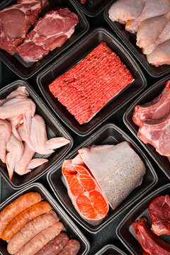 Top view. Set of fresh raw meat and fish. In black plastic containers. Products from the market. Vertical photo.