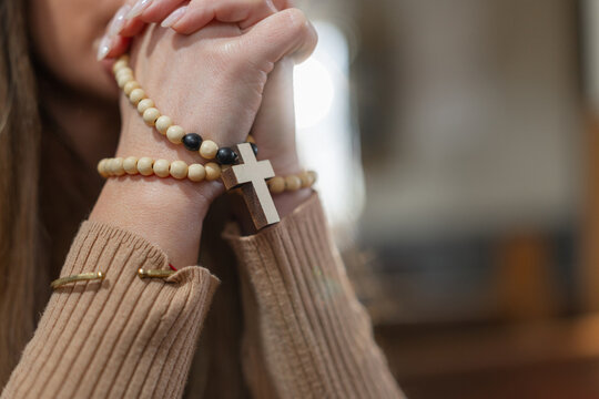A woman prays in a European Catholic church during Holy Mass, showing her faith and devotion with clasped hands and a rosary.