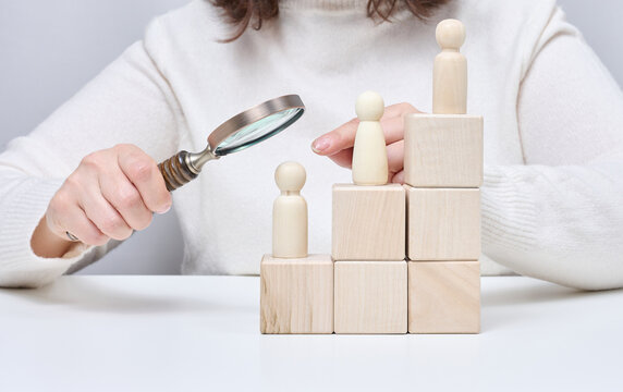 A man with a magnifying glass examines wooden figures on cubes in the form of growth steps.