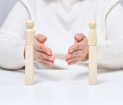 A man uses his hands to bring together two wooden figures on stands, symbolizing negotiators.