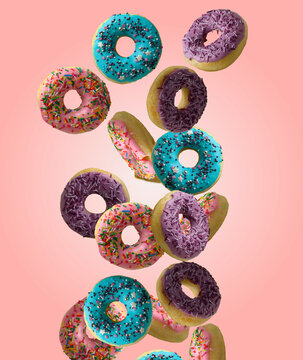 Multicolored donuts with icing and sprinkles float in the air against a pink background.
