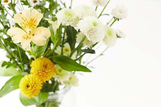 Macro shot of a yellow alstroemeria with red speckles, surrounded by yellow santini and white daisy chrysanthemums. Fresh floral arrangement on a light background.