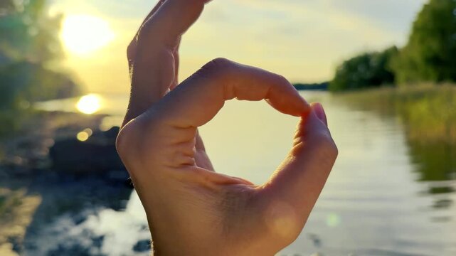 Hand Framing the Low Sun Above Reeds by a Lake Shore