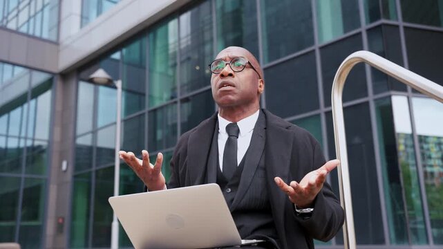 Person discusses topic while sitting outside a building with a laptop during daytime