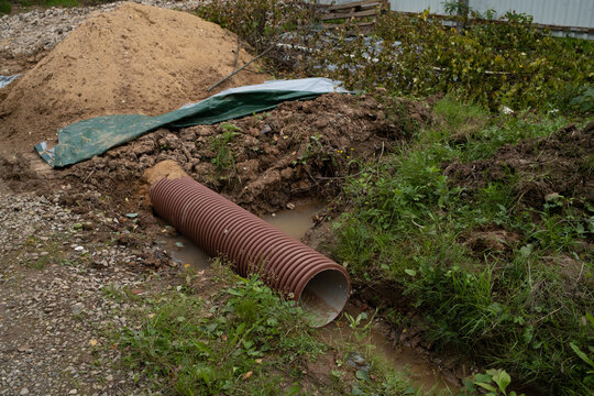 Underground drainage tube partially covered with soil in ditch outdoors, pipeline backfilling process, earthworks improvement, construction phase.