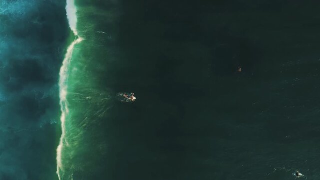 Cinematic aerial tracking of surfers in turquoise ocean water below Jaran Hill in Uluwatu Bali &ndash; Breathtaking bright daylight illuminating tropical sea surf lineup, commercial stock video 4k UHD asset