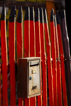 View of a rustic wooden fence painted in vibrant red with black tips, featuring a weathered metal mailbox attached, with Stara planina in Gostusa, Pirot District, Serbia.
