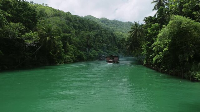 Aerial view of a traditional wooden boat on the emerald green waters of the Loboc River surrounded by lush tropical jungle in Loboc, Central Visayas, Philippines.